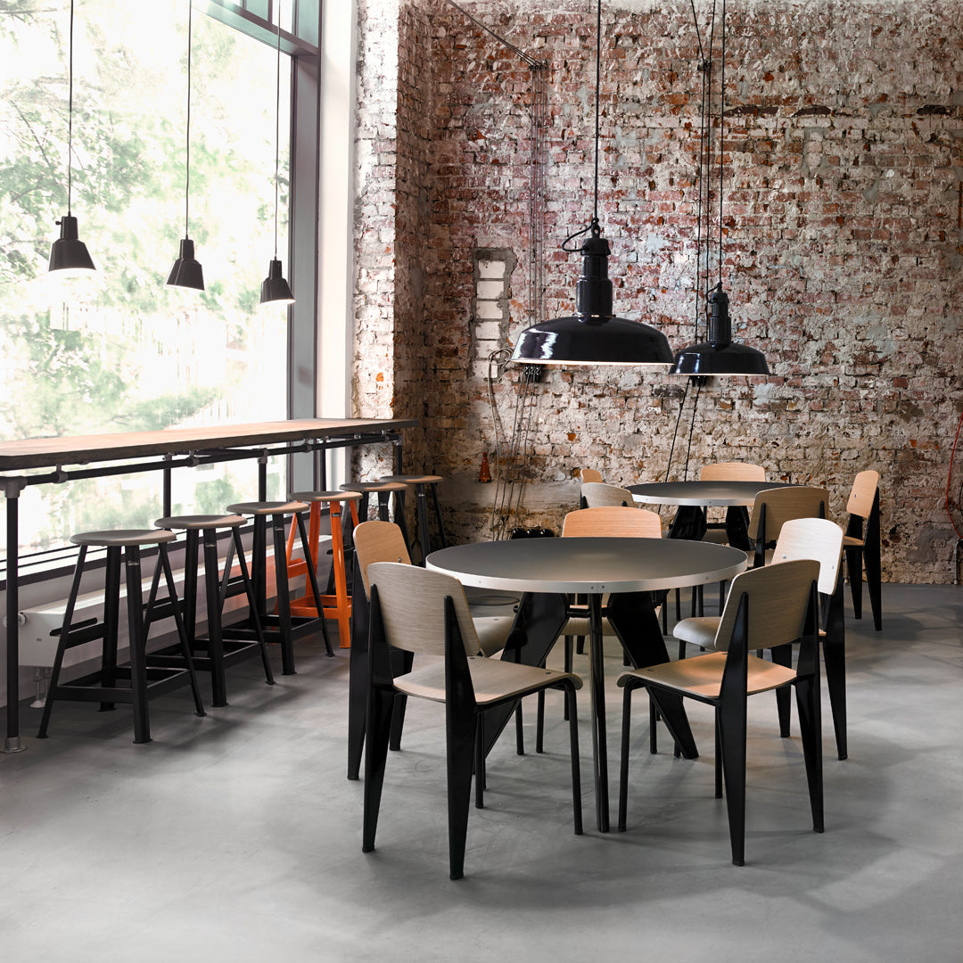 Round black dining table with beige chairs, set against a rustic brick wall and industrial hanging black lights.