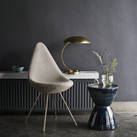 Beige textured chair with gold accents, navy ceramic stool, and muted green vase against a dark gray wall.