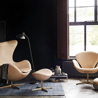 Elegant cream chairs with sleek gold bases, set against a dark backdrop and a textured blue rug.