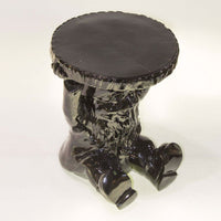 Black ceramic stool with a glossy finish, featuring a unique sculpted design and a textured round top.