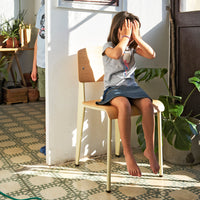 "Light wooden chair with simple design, set against patterned green and white tiled floor in a bright, sunlit room."