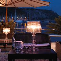 Elegant crystal table lamp with a transparent shade, casting warm golden light against a dark outdoor setting.