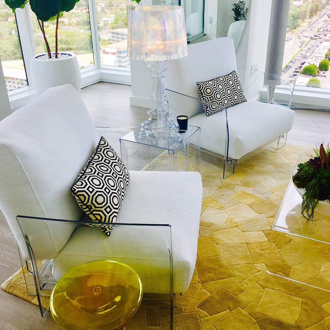 White chairs with black geometric patterned cushions on a yellow hexagonal rug in a bright, modern setting.