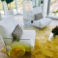 White chairs with black geometric patterned cushions on a yellow hexagonal rug in a bright, modern setting.