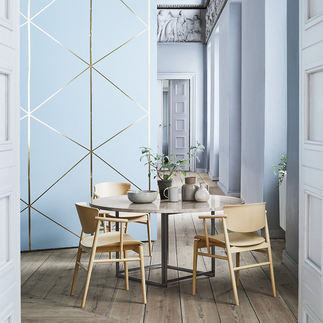 Light blue wall with gold geometric patterns, natural wood flooring, and beige chairs create a serene, modern aesthetic.