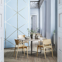 Light blue wall with gold geometric patterns, natural wood flooring, and beige chairs create a serene, modern aesthetic.