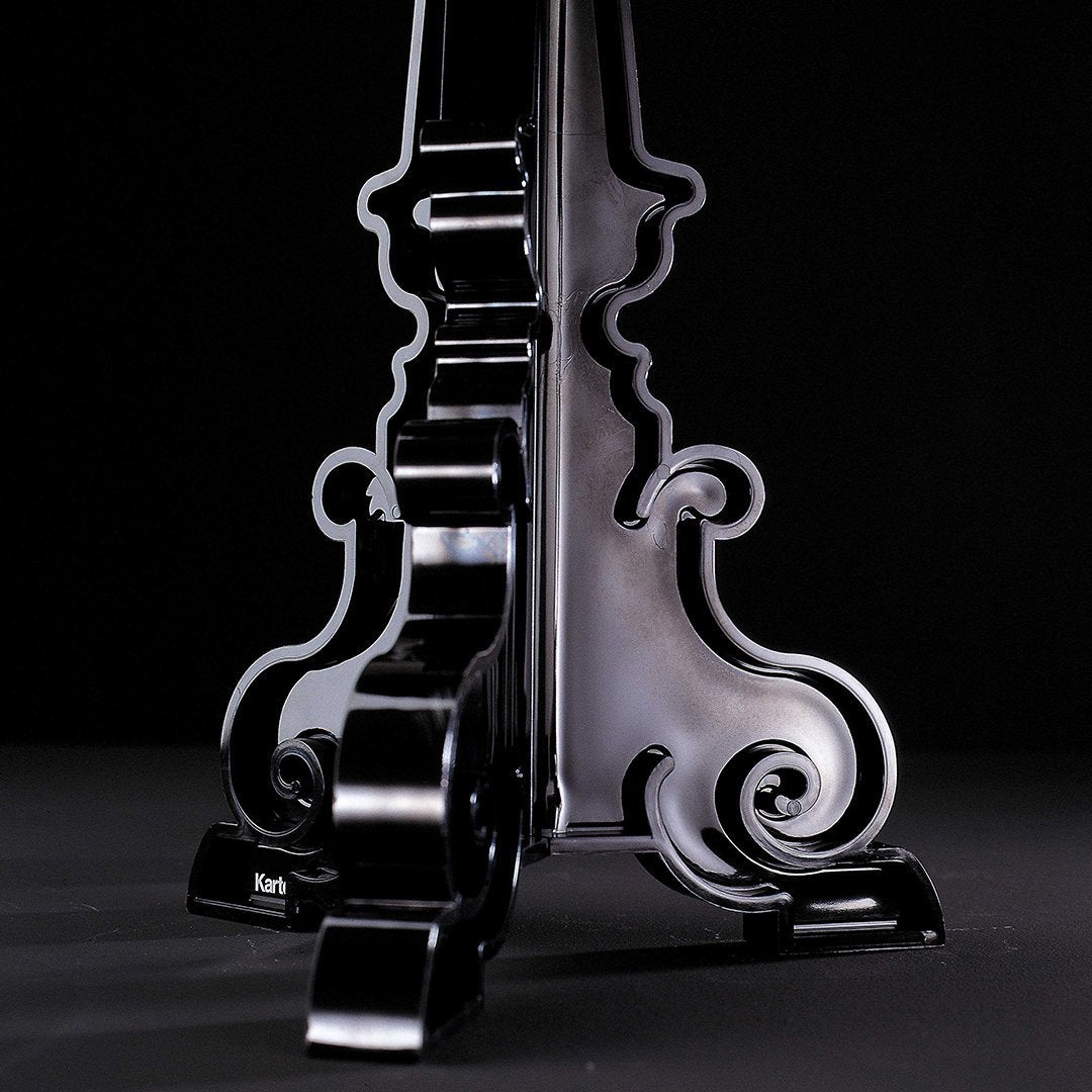 Glossy black stand with intricate scrollwork and curvy patterns against a dark background.