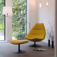 Yellow accent chair with smooth, modern contours, paired with a matching ottoman and sleek black base in a bright room.