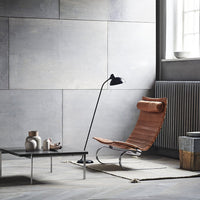 Modern lounge chair with brown leather and sleek silver accents in a minimalist gray interior setting.