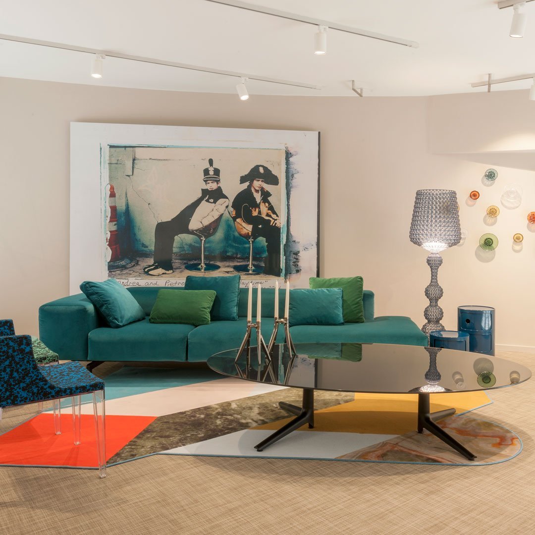 Teal sectional sofa with green accent pillows, geometric patterned rug, and colorful art. Modern, vibrant living space.