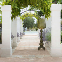 Green textured lamp with intricate mesh pattern, set against a serene outdoor backdrop of lavender and stone walkways.