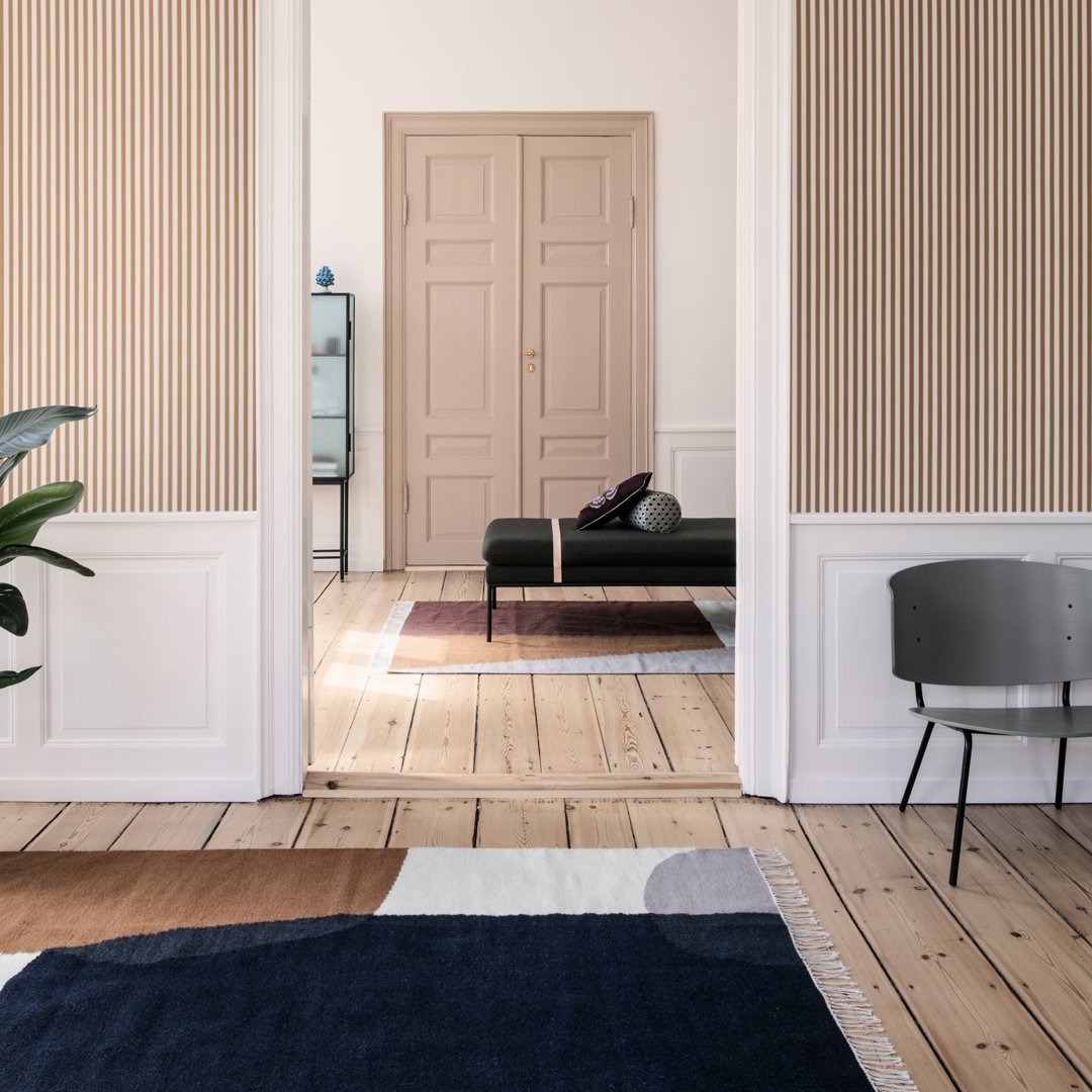 Navy blue, beige, and soft gray geometric patterned rug on wooden floor in a modern interior setting.