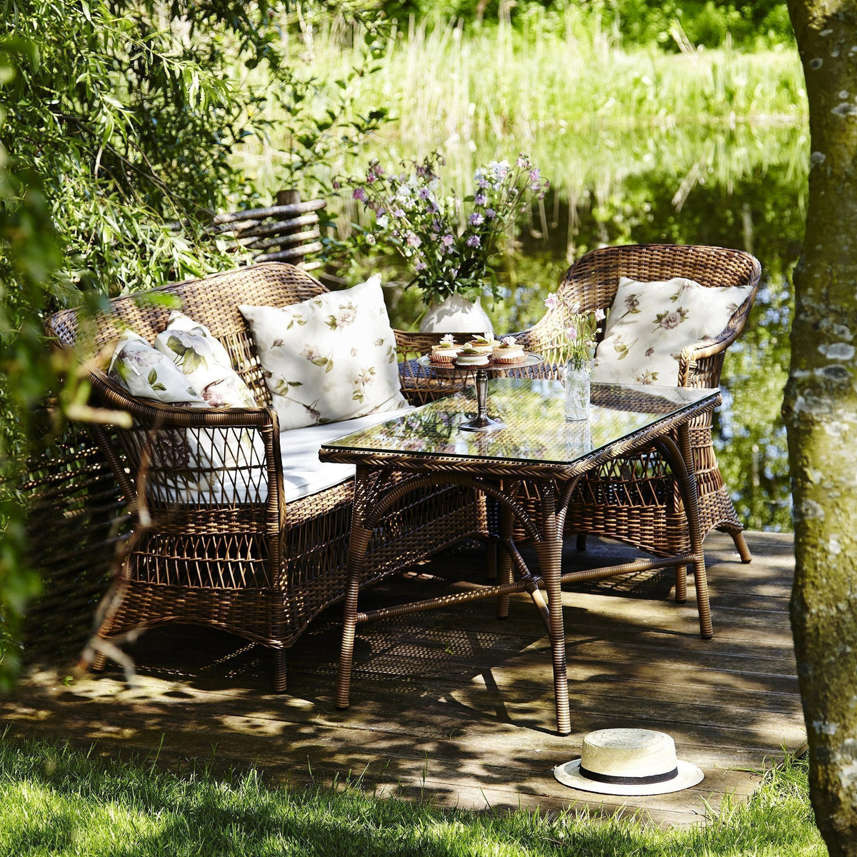 Natural wicker outdoor seating set with floral-patterned cushions and a glass table, surrounded by greenery.