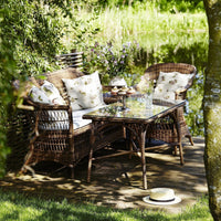 Natural wicker outdoor seating set with floral-patterned cushions and a glass table, surrounded by greenery.