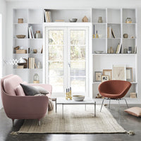 Soft pink sofa and warm orange chair contrast against neutral tones in a minimalist, modern living room.
