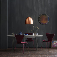 Modern dining set featuring deep burgundy chairs and a sleek white table, accented by a copper pendant light.