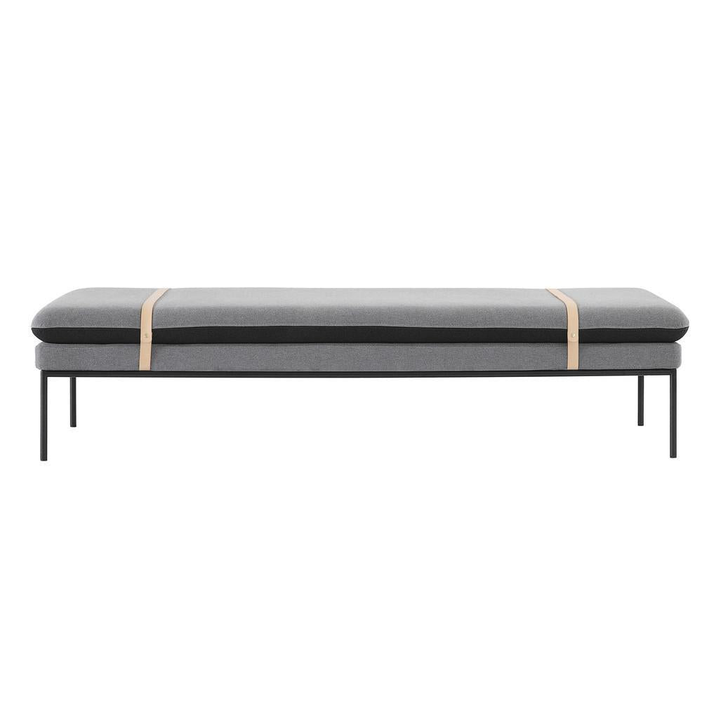 Gray and black padded bench with minimalist design and tan accent straps, set on a sleek black metal frame.