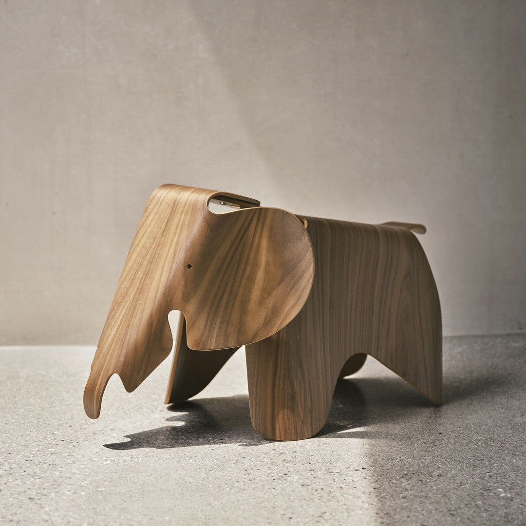 Wooden elephant figurine in warm brown tones, featuring smooth, curved lines and natural wood grain patterns.