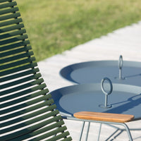 Green slatted chair beside blue circular tables with wooden accents on a grassy outdoor setting.