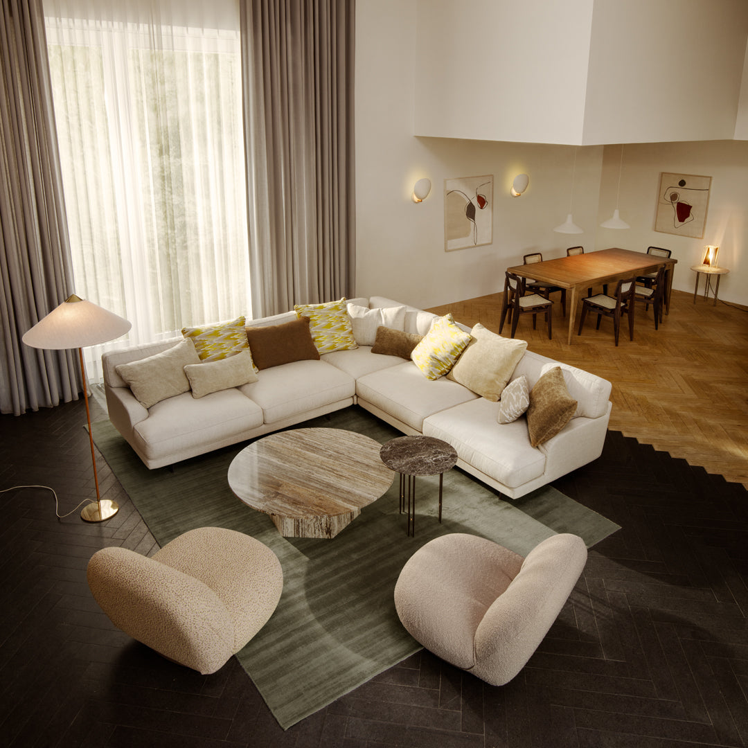 Modern living room featuring a creamy sectional sofa with patterned yellow, green, and brown pillows on a textured green rug.