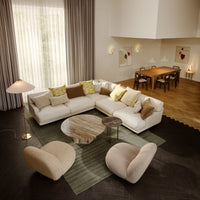 Modern living room featuring a creamy sectional sofa with patterned yellow, green, and brown pillows on a textured green rug.