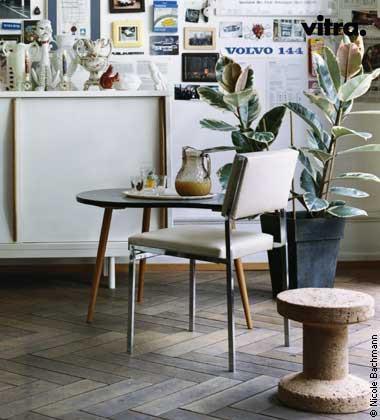 Minimalist white chair with gray upholstery against warm wood tones and patterned floor tiles. Green leaves add a natural touch.