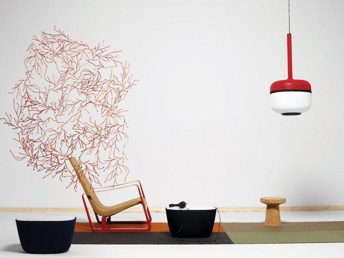 Colorful interior scene featuring a beige rocking chair, red pendant light, and varied patterned rugs in earthy tones.