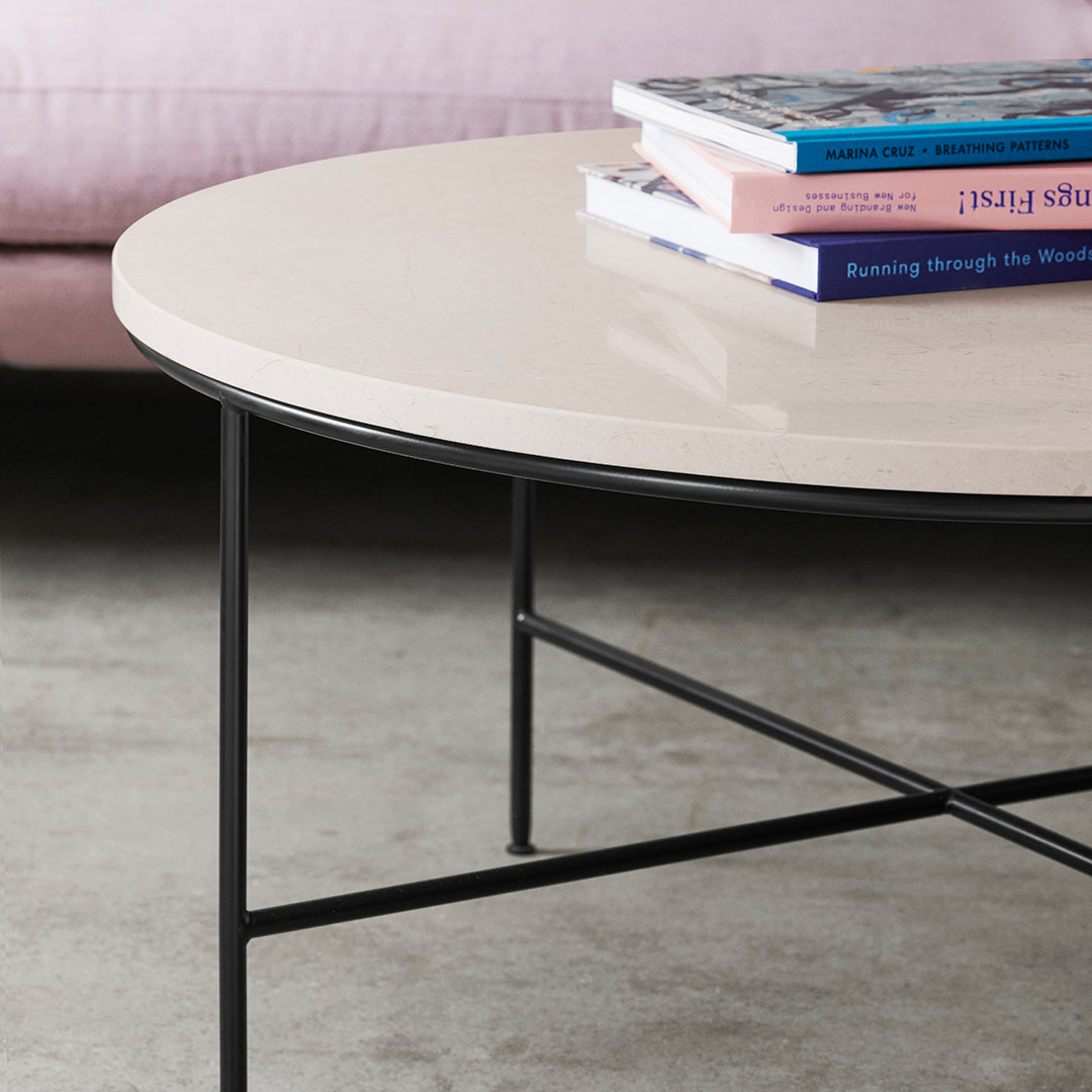 Round beige coffee table with a smooth surface and black metal legs, featuring stacked colorful books on top.