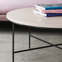 Round beige coffee table with a smooth surface and black metal legs, featuring stacked colorful books on top.