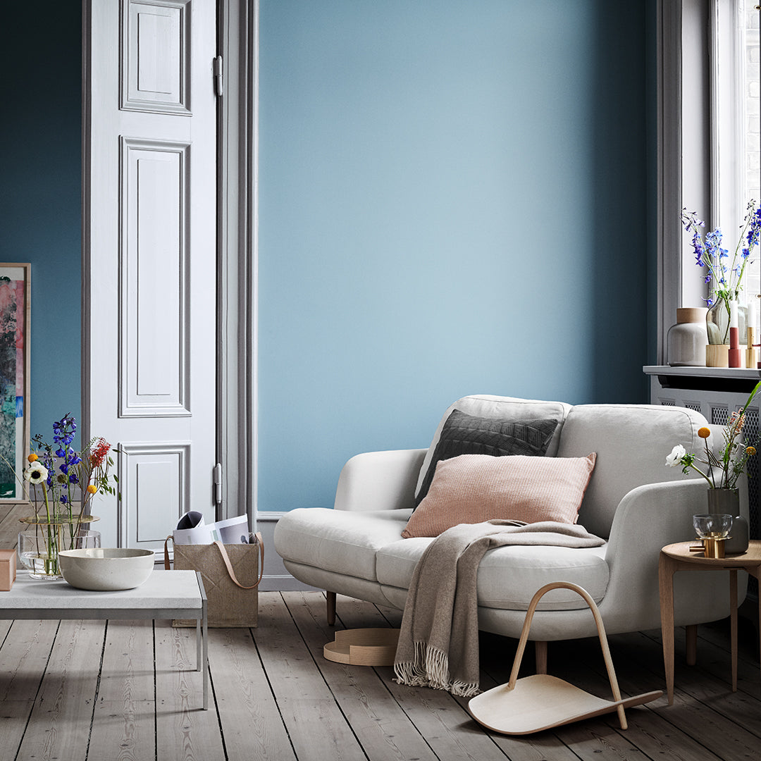 Light blue wall with soft white sofa, pastel pink and gray accents, and natural wood flooring adorned with floral decor.