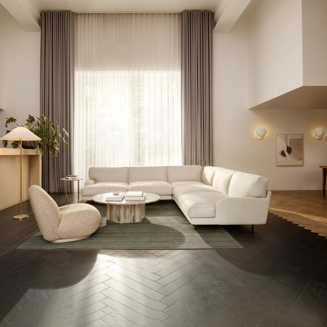 Light beige sectional sofa on dark herringbone floor, with soft gray curtains and a round patterned rug.