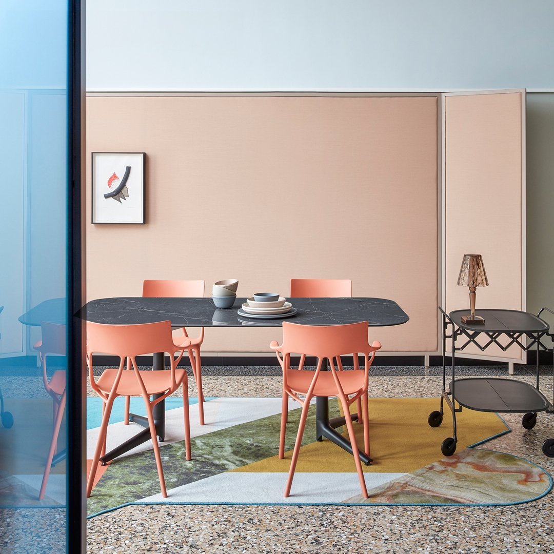 Modern dining space featuring coral chairs, a dark tabletop, and a colorful patterned rug with earthy tones.
