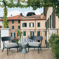 Black chairs with striped gray cushions, a gray table, and a backdrop of pastel-colored buildings and green foliage.
