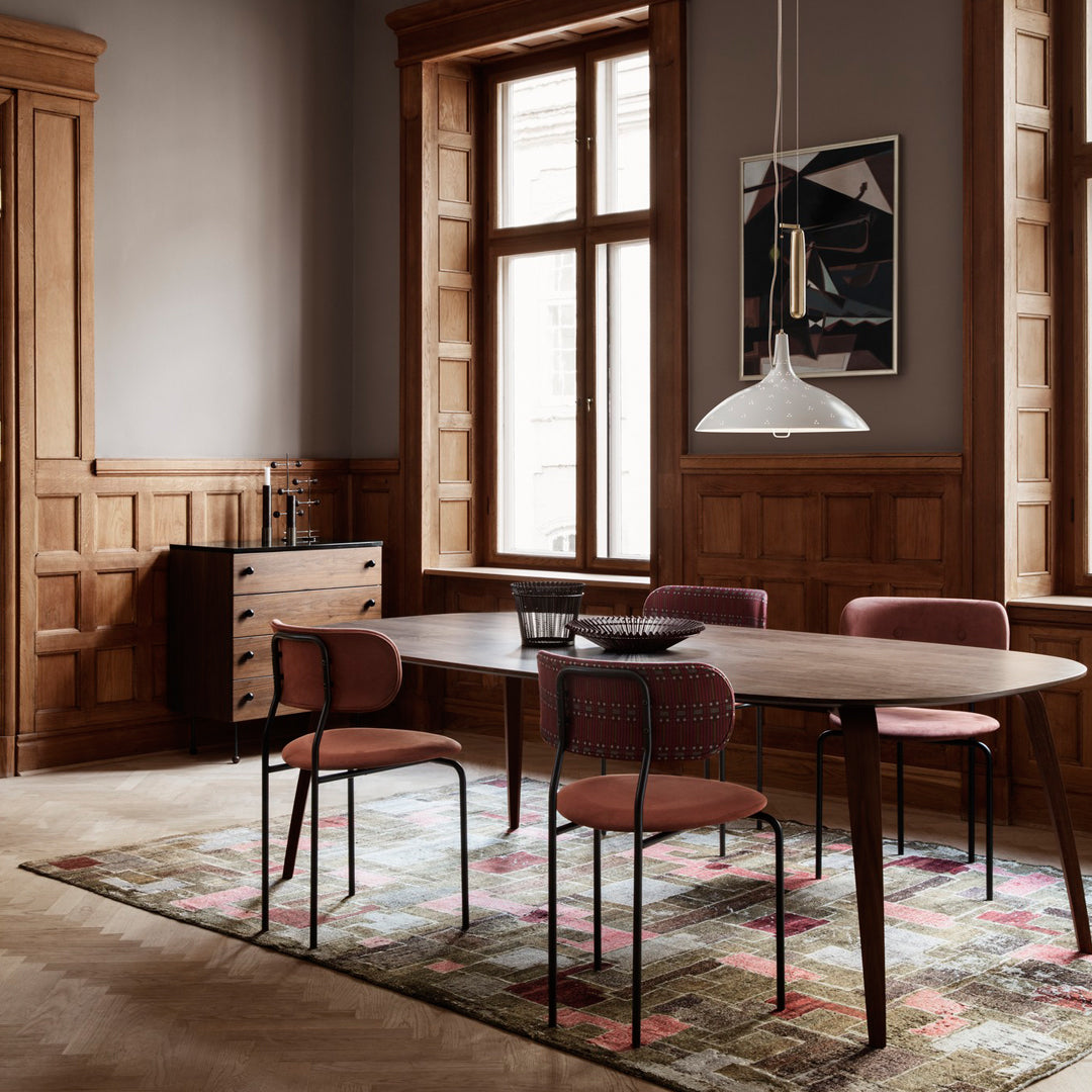 Modern dining room featuring a round table, burgundy chairs, and a multicolored patterned rug on a light wood floor.