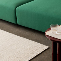 Green upholstered sofa with textured beige rug and maroon accent table. Modern, clean lines for stylish decor.