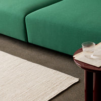Green fabric couch with a textured, natural fiber rug in a neutral cream color, set on a dark floor.