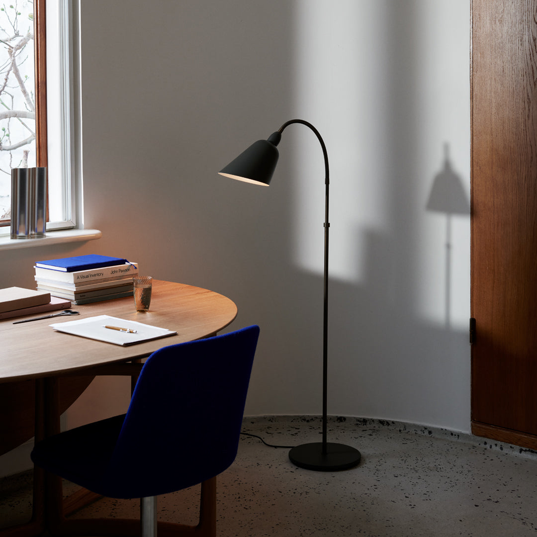 Black floor lamp with a sleek design, set against a light gray wall, complemented by a warm light shadow and blue chair.