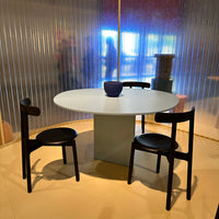 Modern round dining table with a sleek white surface, complemented by matte black chairs in a chic, minimalist setting.