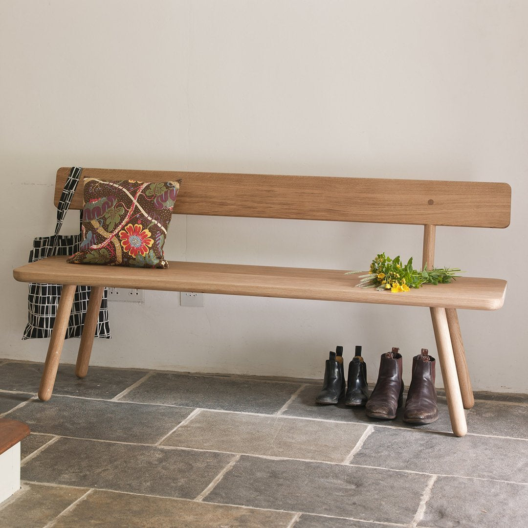 Natural wood bench with a colorful patterned pillow, classic design against a neutral wall and stone floor.