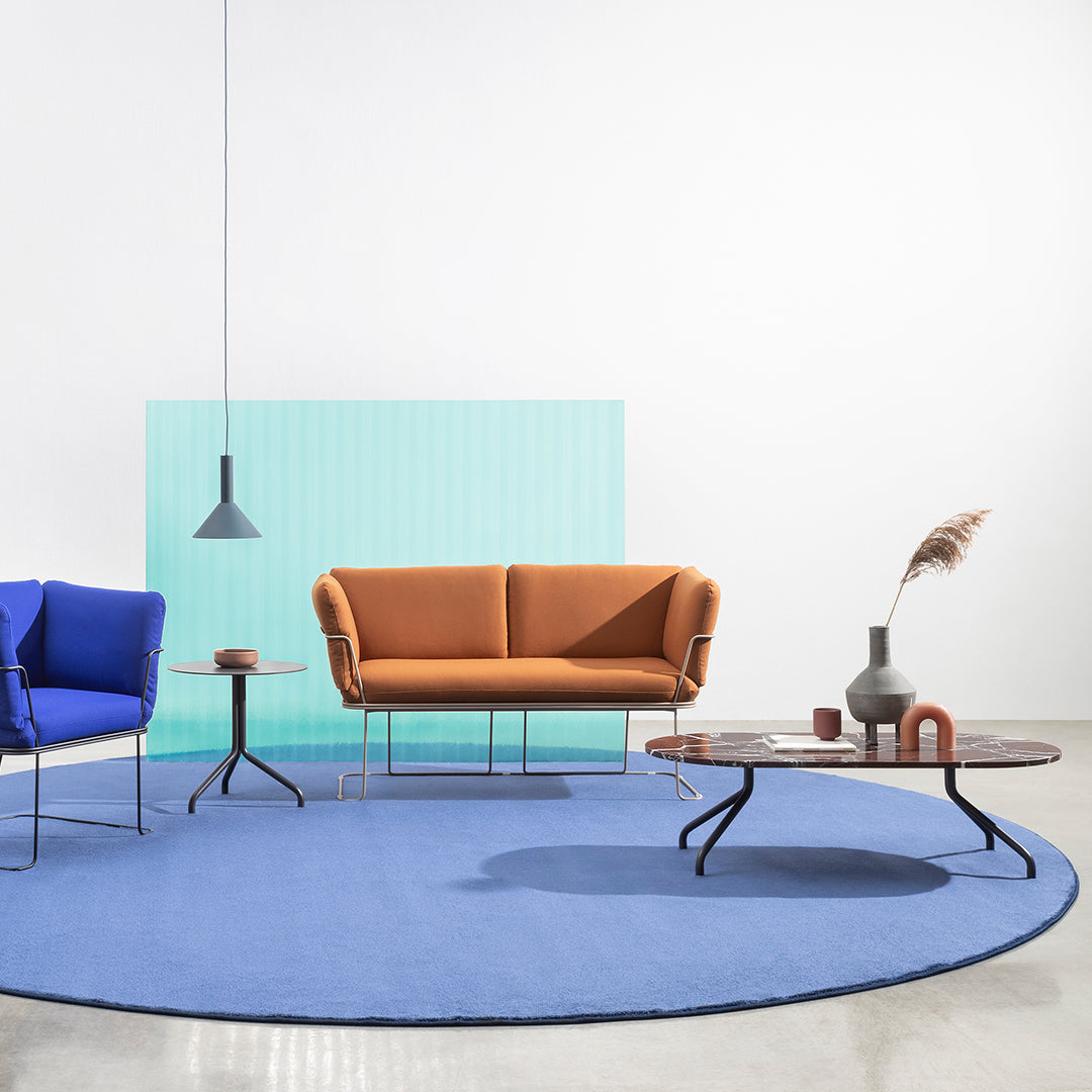 Bright orange sofa, deep blue round rug, and teal accent wall create a modern, vibrant living space.