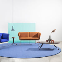 Orange sofa paired with blue armchairs on a round blue rug, complemented by a green backdrop and sleek black table.