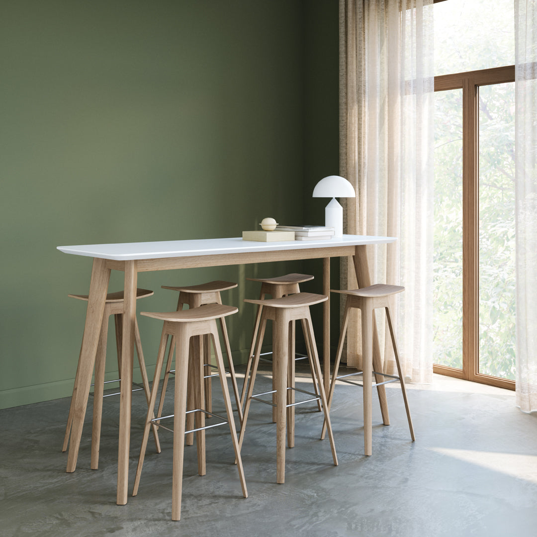 Modern white bar table with natural wood legs and matching stools against a muted green wall. Bright and airy design.