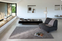 Gray upholstered chair on a patterned gray rug in a modern, minimalist living room with black coffee table and natural light.