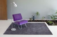 Purple velvet chair on a geometric-patterned dark gray rug in a modern interior setting.