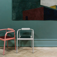 Modern chairs in blush pink and light gray against a deep teal wall with geometric artwork in rich reds and yellows.