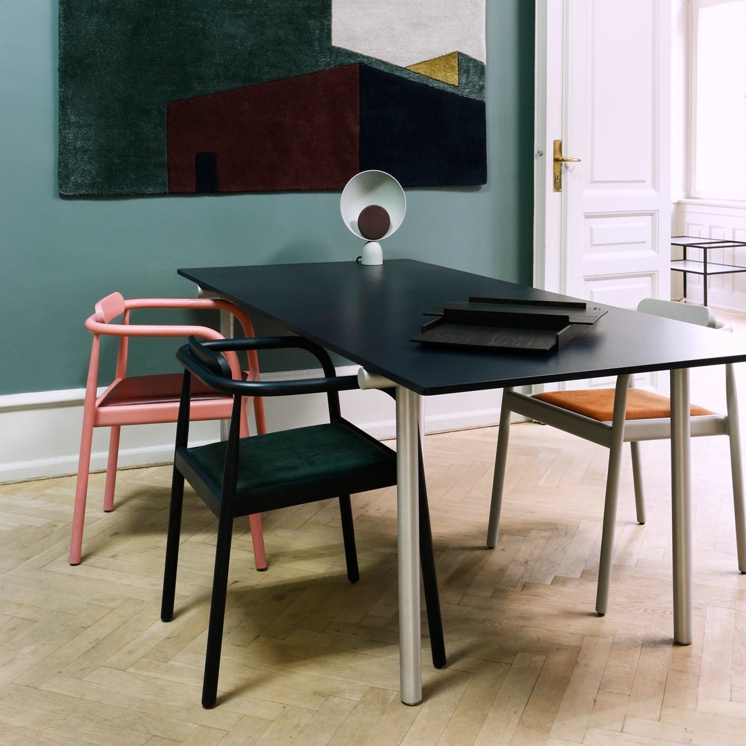 Modern dining table with black surface and colorful chairs: pink, green, black, and orange on a light wood floor.