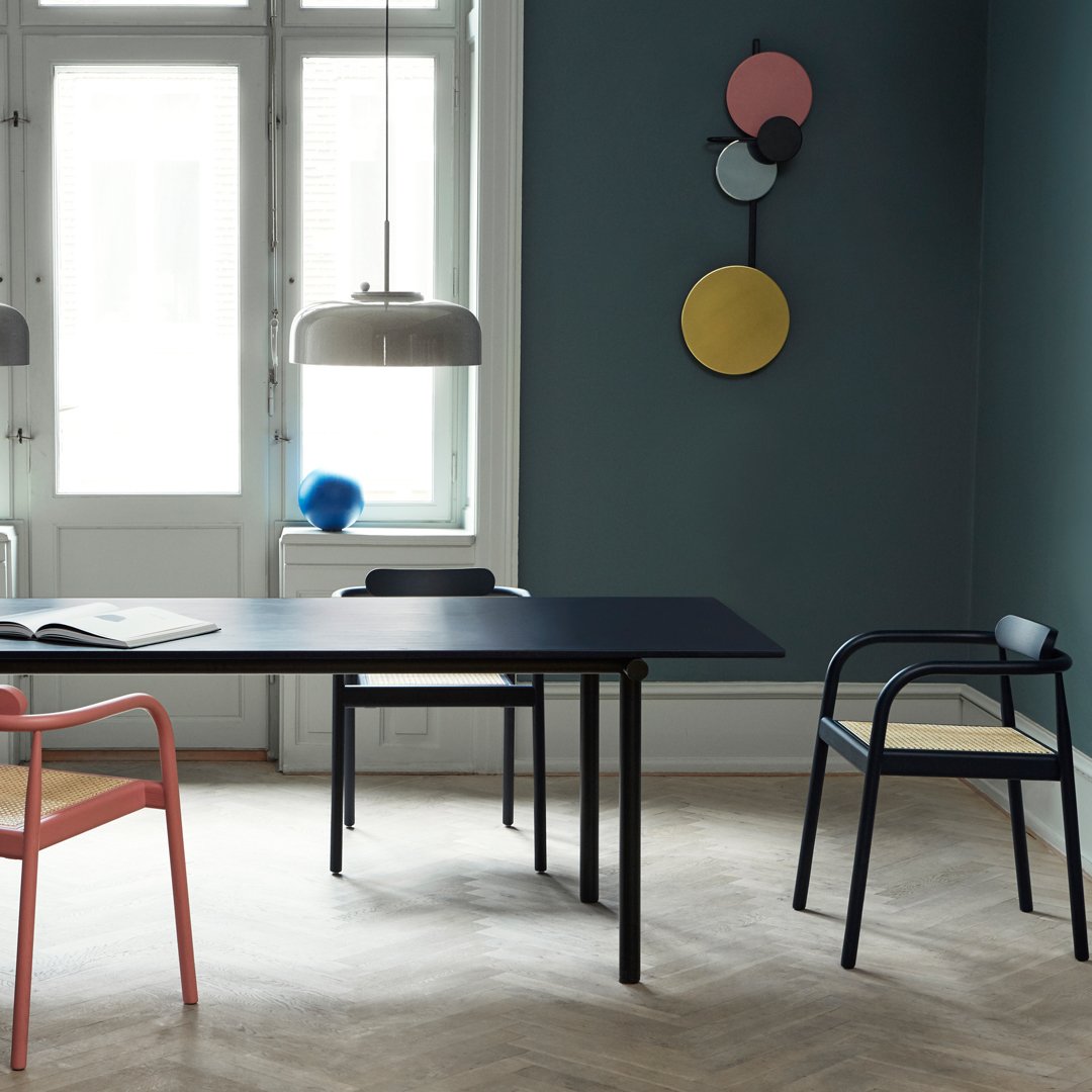 Modern living space featuring a dark blue table, pink and black chairs, and colorful wall decor on a muted green background.