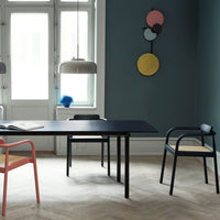 Modern living space featuring a dark blue table, pink and black chairs, and colorful wall decor on a muted green background.