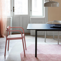 Modern pink chair with a black table on a textured pink rug, featuring soft pastel tones and natural light.