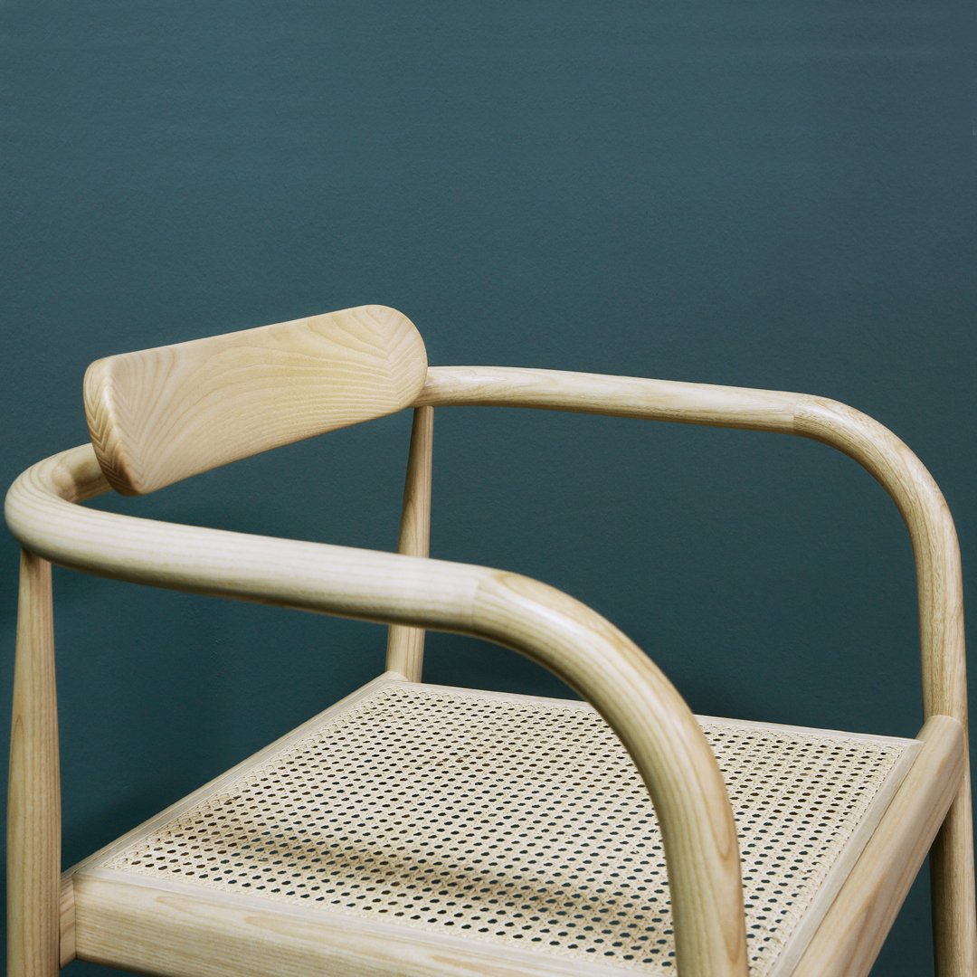 Natural wood color chair with a woven cane seat against a deep green background, showcasing minimalist design.